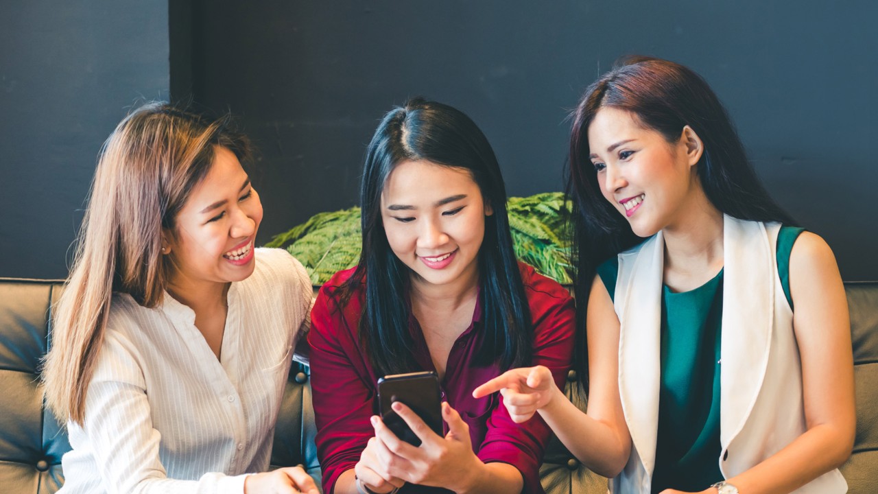 Three female friends using a phone on couch; image used for HSBC Philippines Credit Cards Features Text Alert page