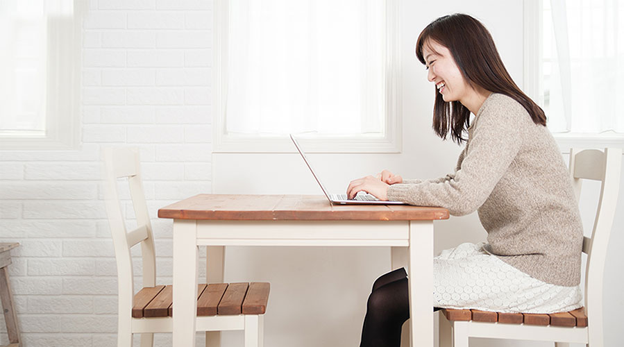 Woman sitting at dining table on computer; image used for HSBC Philippines What Can I Afford article page