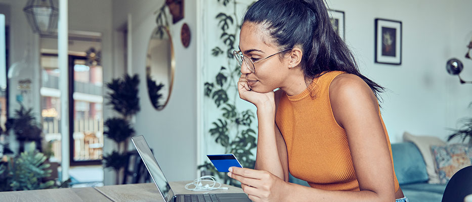 Woman using her laptop while holding her credit card; Image for 'How to transfer credit card balance to another card?' article