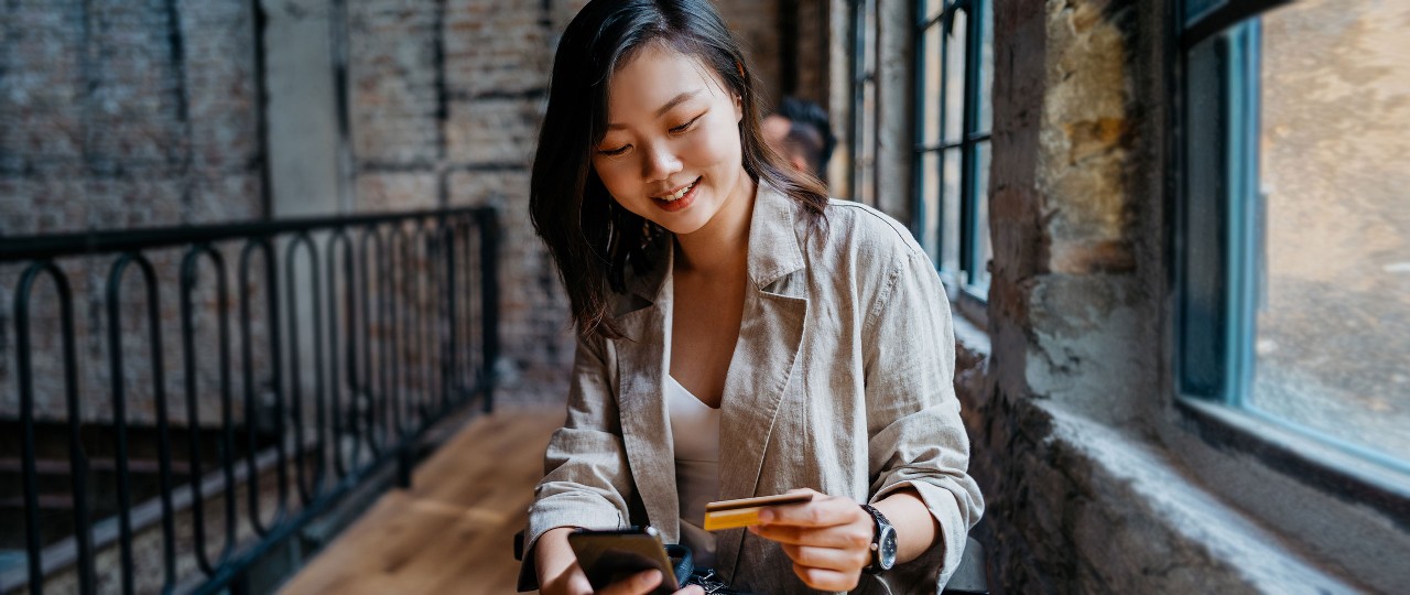 Woman using her phone and credit card; Image for 'How to use credit card' article