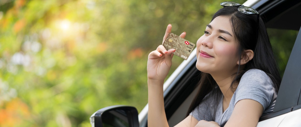 Woman in her car, showing her credit card; Image for 'Cashback credit card' article