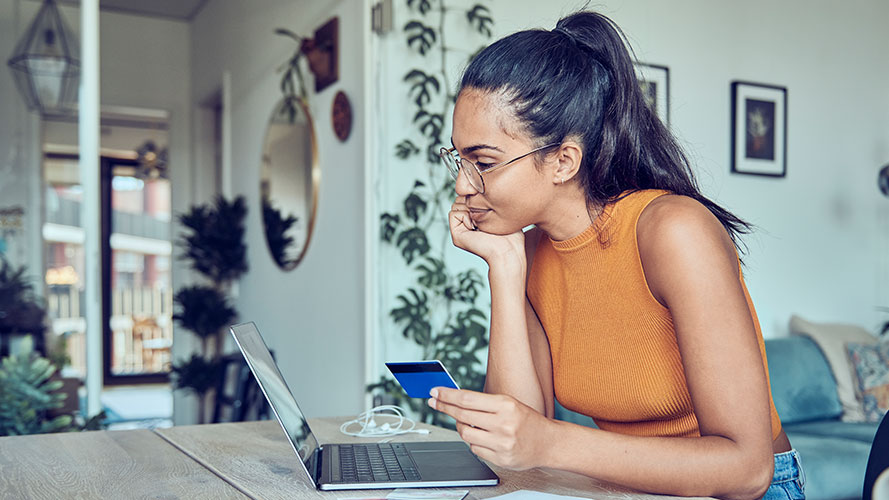 Woman using her laptop while holding her credit card; Image for 'How to transfer credit card balance to another card?' article