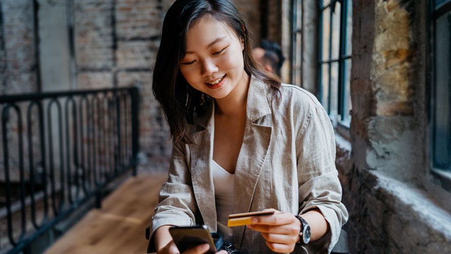 Woman using her phone and credit card; Image for 'How to use credit card' article