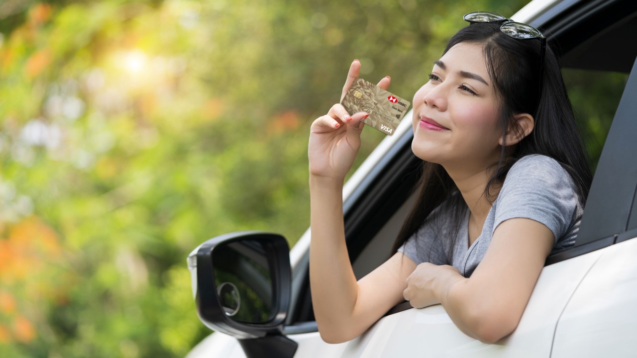 Woman in her car, showing her credit card; Image for 'Cashback credit card' article