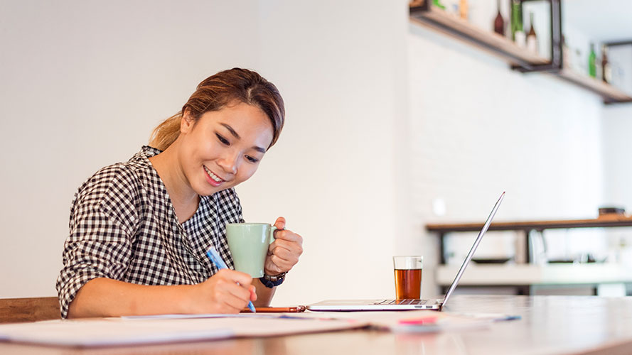 Woman drinking coffee and writing at her table; image used for HSBC Philippines