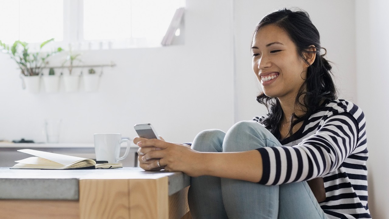 women sitting in the kitchen on phone; image used for HSBC Philippines Mobile Banking page